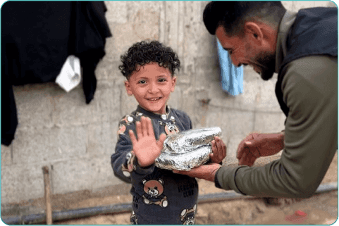 طفل فلسطيني نازح يبتسم بفرح أثناء استلامه وجبة ساخنة